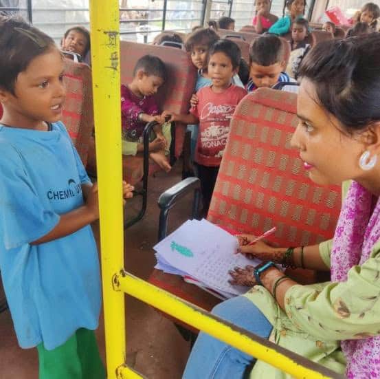 A teacher from Aasraa Trust guides a student in a recitation exercise inside the Mobile Learning Centre bus in Dehradun.